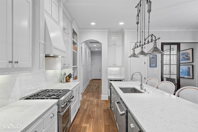 kitchen with decorative light fixtures, white cabinetry, sink, stainless steel range, and light stone counters