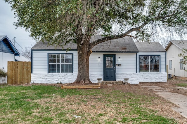 single story home with stone siding, roof with shingles, a front yard, and fence