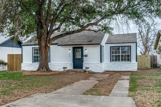 ranch-style home with a shingled roof, cooling unit, stone siding, and fence