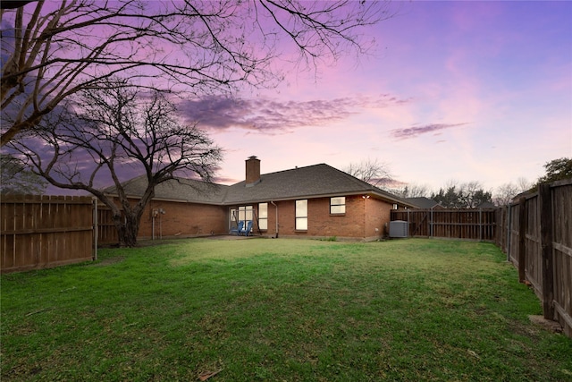 back house at dusk with a lawn and central air condition unit