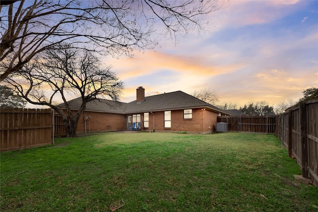 back house at dusk with central AC and a lawn