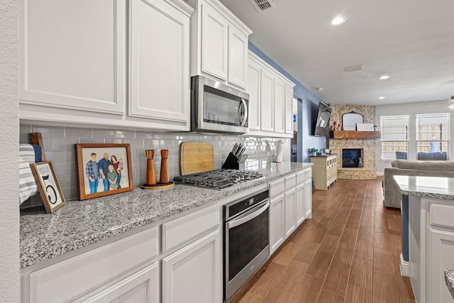 kitchen featuring white cabinetry, stainless steel appliances, a stone fireplace, and decorative backsplash