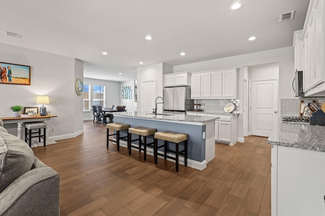 kitchen featuring appliances with stainless steel finishes, dark hardwood / wood-style flooring, a center island with sink, and white cabinets