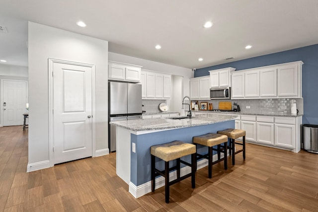 kitchen featuring appliances with stainless steel finishes, an island with sink, sink, white cabinets, and light stone counters