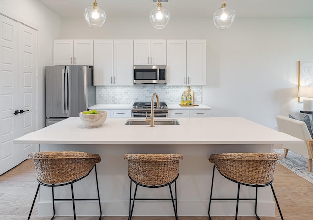 kitchen featuring stainless steel appliances, white cabinetry, sink, and a center island with sink