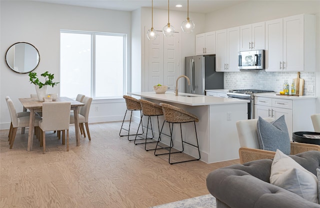 kitchen featuring decorative light fixtures, an island with sink, white cabinets, and appliances with stainless steel finishes