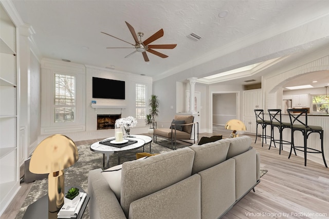 living room featuring crown molding, plenty of natural light, a large fireplace, and light wood-type flooring