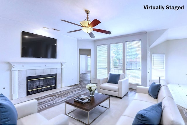 living room featuring a tiled fireplace, light hardwood / wood-style flooring, ornamental molding, and ceiling fan