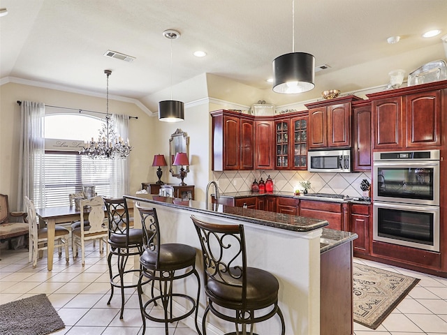 kitchen with lofted ceiling, appliances with stainless steel finishes, decorative light fixtures, and light tile patterned floors