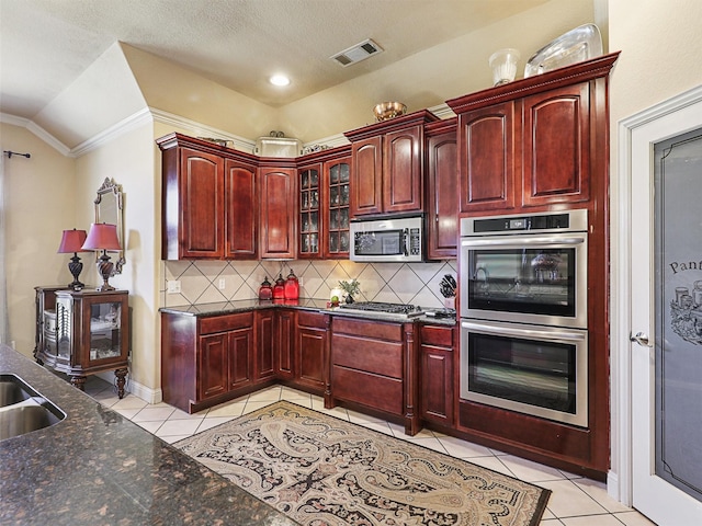 kitchen with light tile patterned flooring, lofted ceiling, dark stone counters, stainless steel appliances, and decorative backsplash