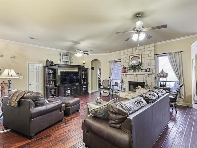 living room with crown molding, a stone fireplace, dark wood-type flooring, and ceiling fan