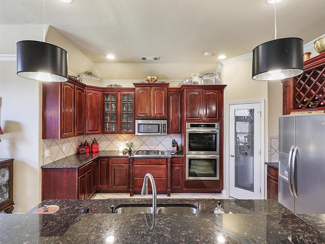 kitchen featuring sink, appliances with stainless steel finishes, hanging light fixtures, backsplash, and dark stone counters