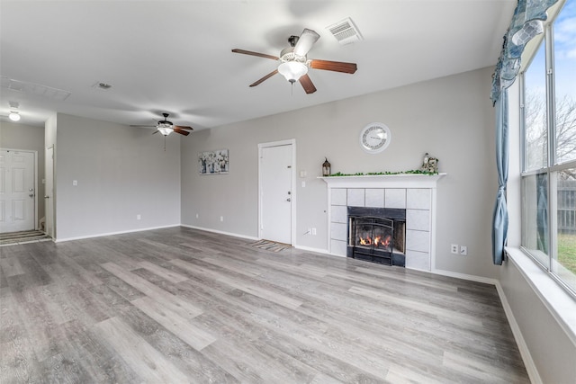 unfurnished living room with a fireplace, plenty of natural light, light hardwood / wood-style floors, and ceiling fan