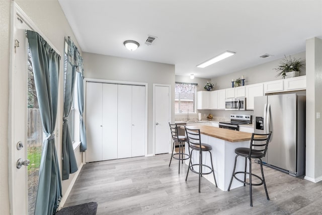 kitchen with butcher block counters, a breakfast bar area, a center island, appliances with stainless steel finishes, and white cabinets