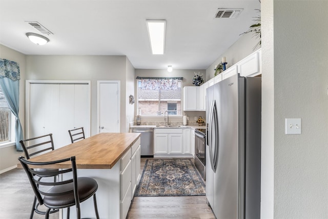 kitchen featuring appliances with stainless steel finishes, sink, white cabinets, wooden counters, and a center island