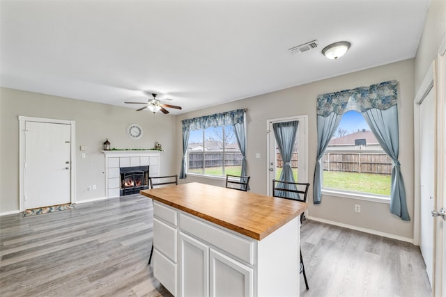 kitchen with wooden counters, light wood-type flooring, a kitchen island, a tiled fireplace, and white cabinets