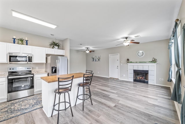 kitchen with a tile fireplace, a breakfast bar, white cabinetry, butcher block counters, and stainless steel appliances