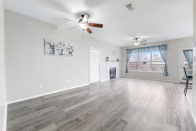 unfurnished living room with a tiled fireplace, hardwood / wood-style floors, and ceiling fan