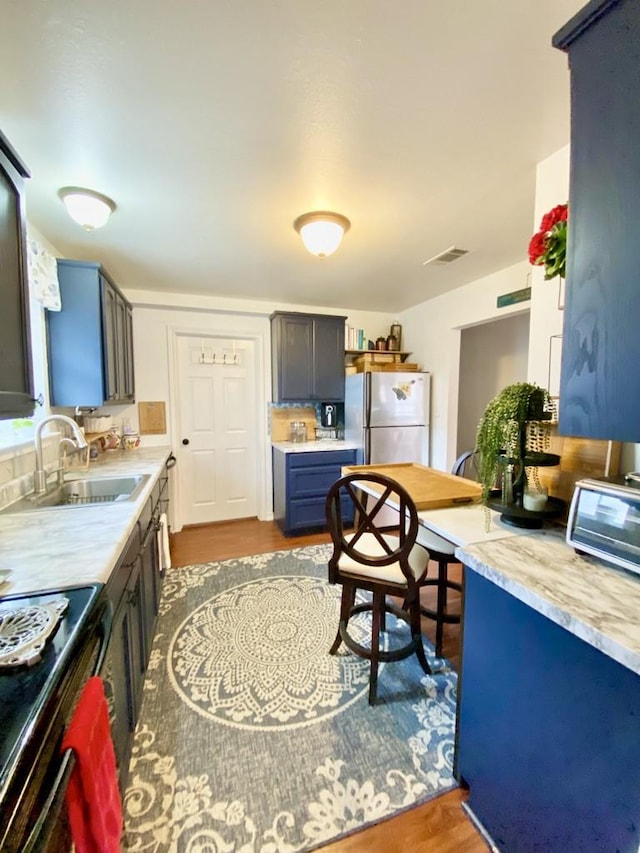 kitchen featuring hardwood / wood-style flooring, range with electric cooktop, sink, and stainless steel refrigerator