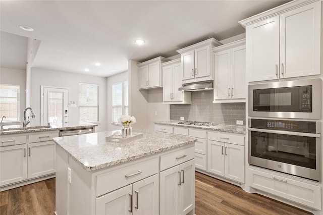 kitchen with a kitchen island, appliances with stainless steel finishes, white cabinetry, sink, and light stone counters