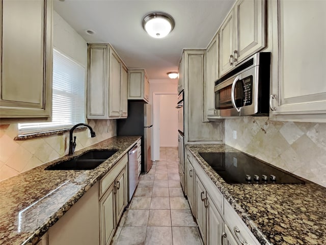 kitchen featuring sink, dark stone countertops, appliances with stainless steel finishes, decorative backsplash, and cream cabinetry