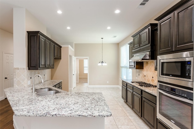 kitchen with sink, dark brown cabinets, stainless steel appliances, tasteful backsplash, and light stone counters