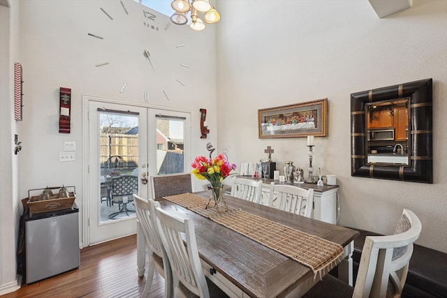 dining area with a high ceiling, a notable chandelier, dark hardwood / wood-style flooring, and french doors