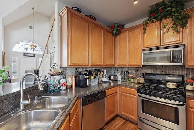 kitchen with vaulted ceiling, decorative light fixtures, sink, backsplash, and stainless steel appliances