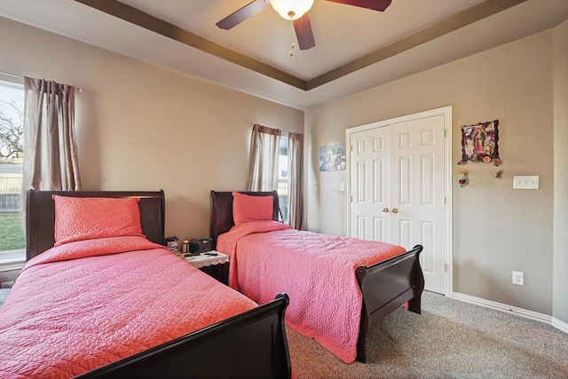 carpeted bedroom featuring a raised ceiling, a closet, and ceiling fan