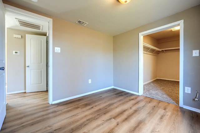 unfurnished bedroom featuring a spacious closet, a closet, and light wood-type flooring