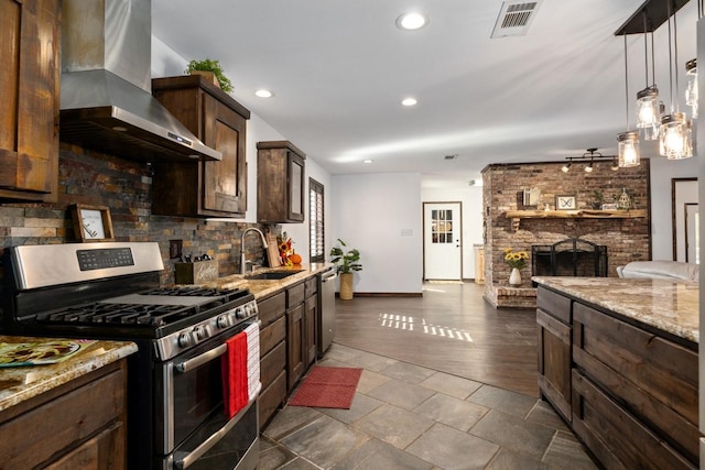 kitchen with wall chimney exhaust hood, sink, a brick fireplace, pendant lighting, and stainless steel appliances