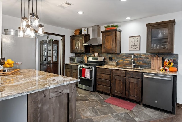 kitchen with wall chimney range hood, sink, dark brown cabinets, stainless steel appliances, and decorative light fixtures