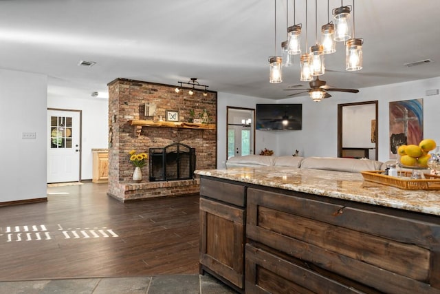 kitchen with ceiling fan, hanging light fixtures, dark hardwood / wood-style floors, a fireplace, and light stone countertops