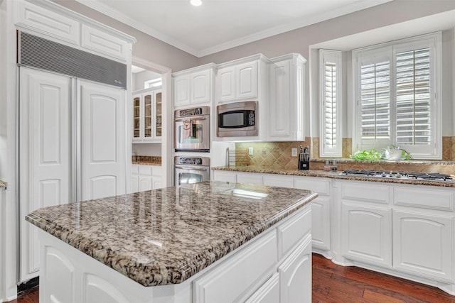 kitchen with ornamental molding, a center island, built in appliances, and white cabinets