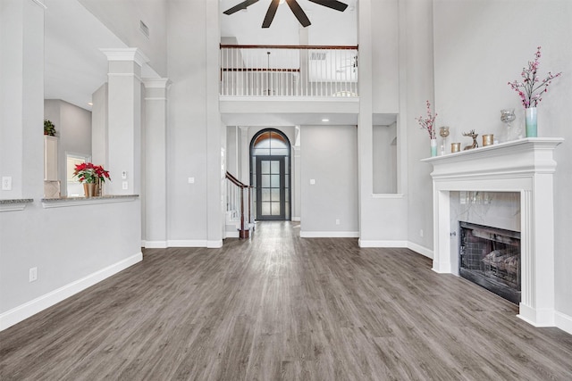 unfurnished living room with hardwood / wood-style floors, a towering ceiling, a high end fireplace, and ceiling fan