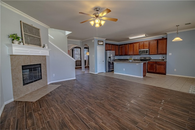 kitchen featuring hanging light fixtures, a center island with sink, dark hardwood / wood-style floors, stainless steel appliances, and a tiled fireplace