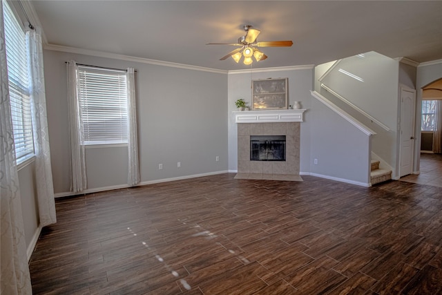 unfurnished living room featuring crown molding, a tile fireplace, dark hardwood / wood-style floors, and ceiling fan