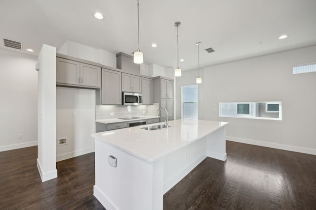 kitchen with sink, gray cabinetry, backsplash, hanging light fixtures, and a center island with sink