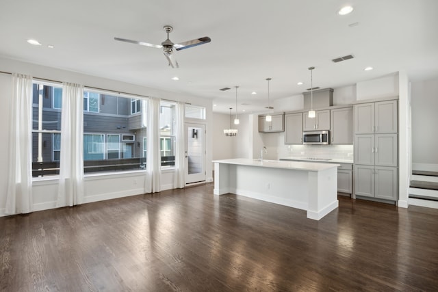 kitchen featuring dark wood-type flooring, an island with sink, hanging light fixtures, and gray cabinetry