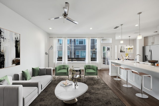 living room with sink, ceiling fan with notable chandelier, and dark wood-type flooring