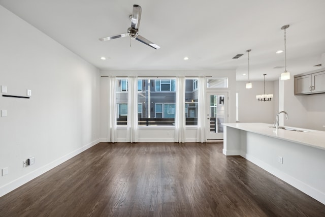 unfurnished living room featuring ceiling fan with notable chandelier, plenty of natural light, dark hardwood / wood-style flooring, and sink