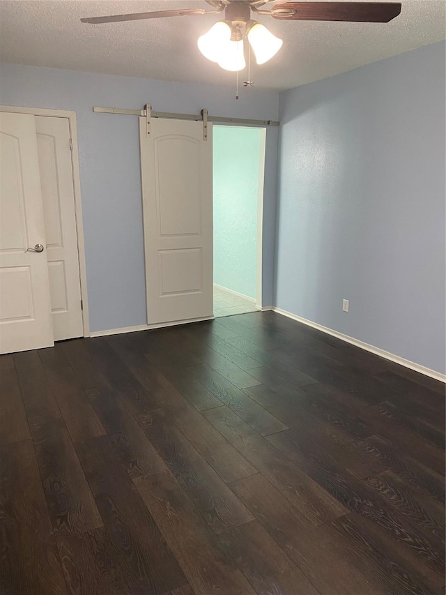 empty room featuring dark wood-type flooring, ceiling fan, a barn door, and a textured ceiling