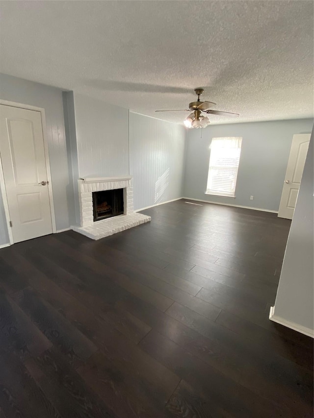 unfurnished living room with dark wood-type flooring, ceiling fan, a brick fireplace, and a textured ceiling