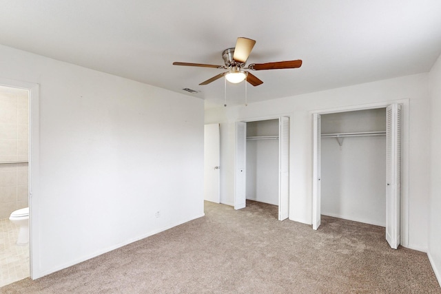 unfurnished bedroom featuring multiple closets, ceiling fan, light colored carpet, and ensuite bath