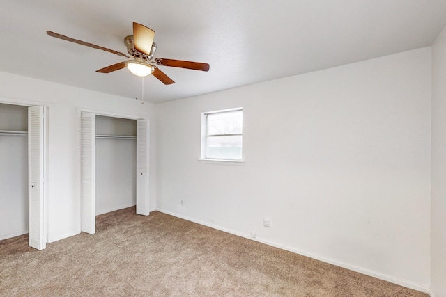 unfurnished bedroom with multiple closets, light colored carpet, and ceiling fan