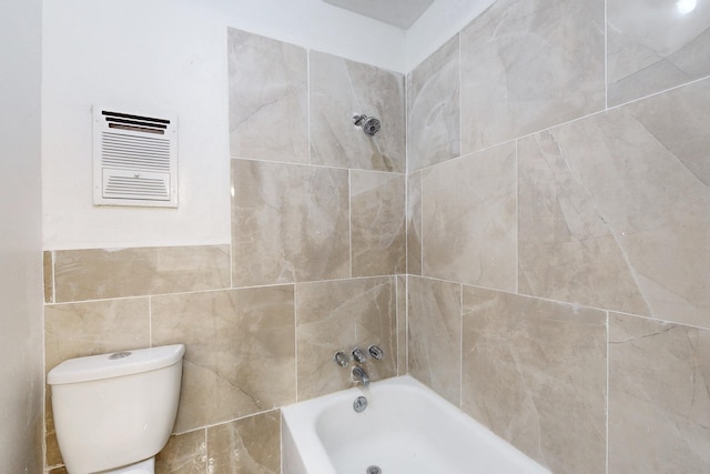 bathroom with tile walls, tiled shower / bath, and toilet