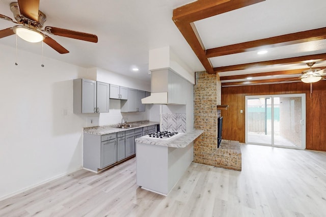 kitchen with sink, light hardwood / wood-style floors, kitchen peninsula, and wood walls