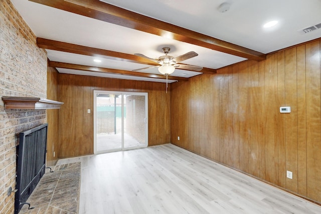 unfurnished living room featuring beam ceiling, wooden walls, and light hardwood / wood-style floors