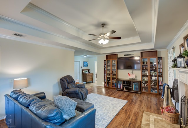 living room with dark wood-type flooring, ornamental molding, and a raised ceiling