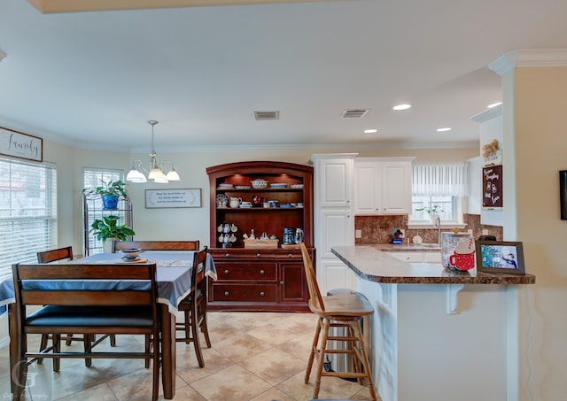 kitchen with tasteful backsplash, hanging light fixtures, crown molding, and a kitchen breakfast bar